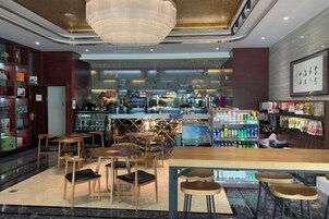 A bar area with seating and a bar counter, a chandelier, and a bartender.