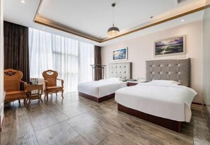 Habitación de hotel con dos camas, una mesa de comedor con sillas, un ventanal con cortinas y un cuadro en la pared.