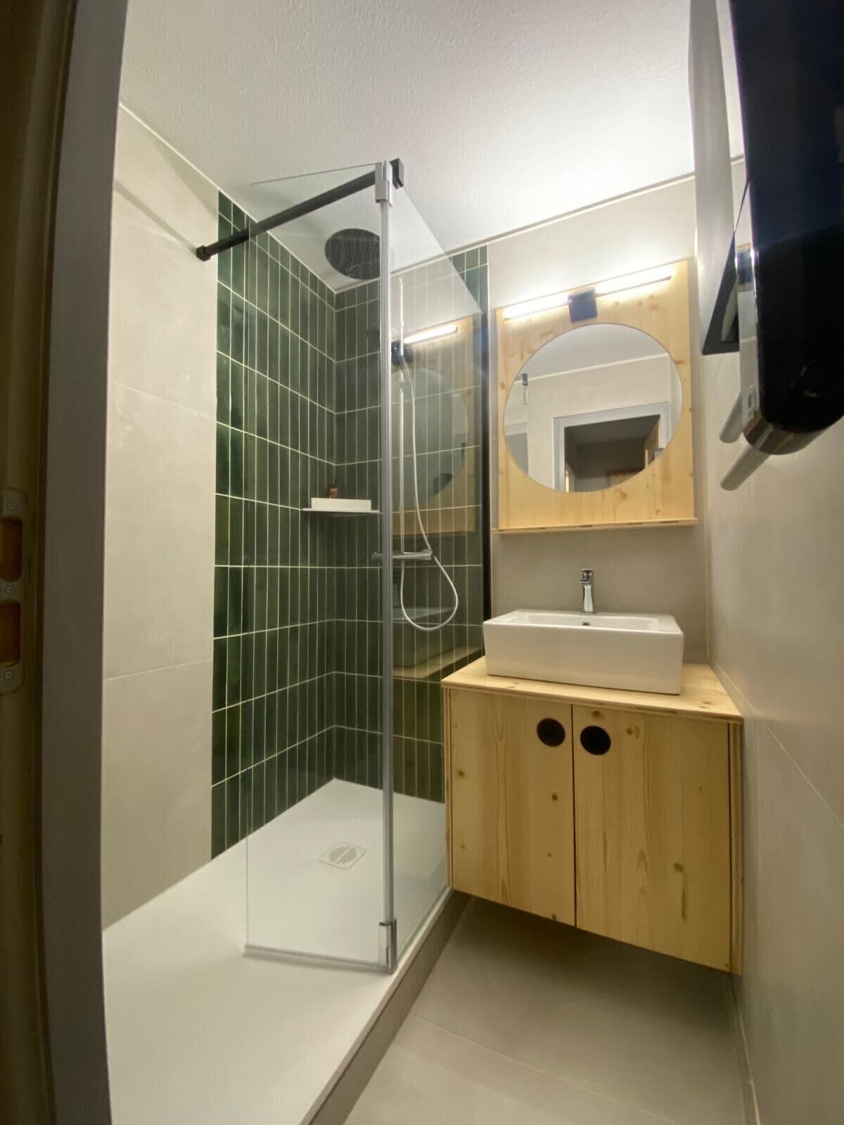 Ein modernes Badezimmer mit einer gläsernen Dusche, einem Holzkosmetikschrank mit Waschbecken und einem Spiegel mit Holzrahmen.