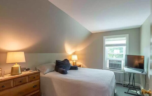 Un dormitorio con cama, lámparas de noche, cómoda, ventana y televisor.