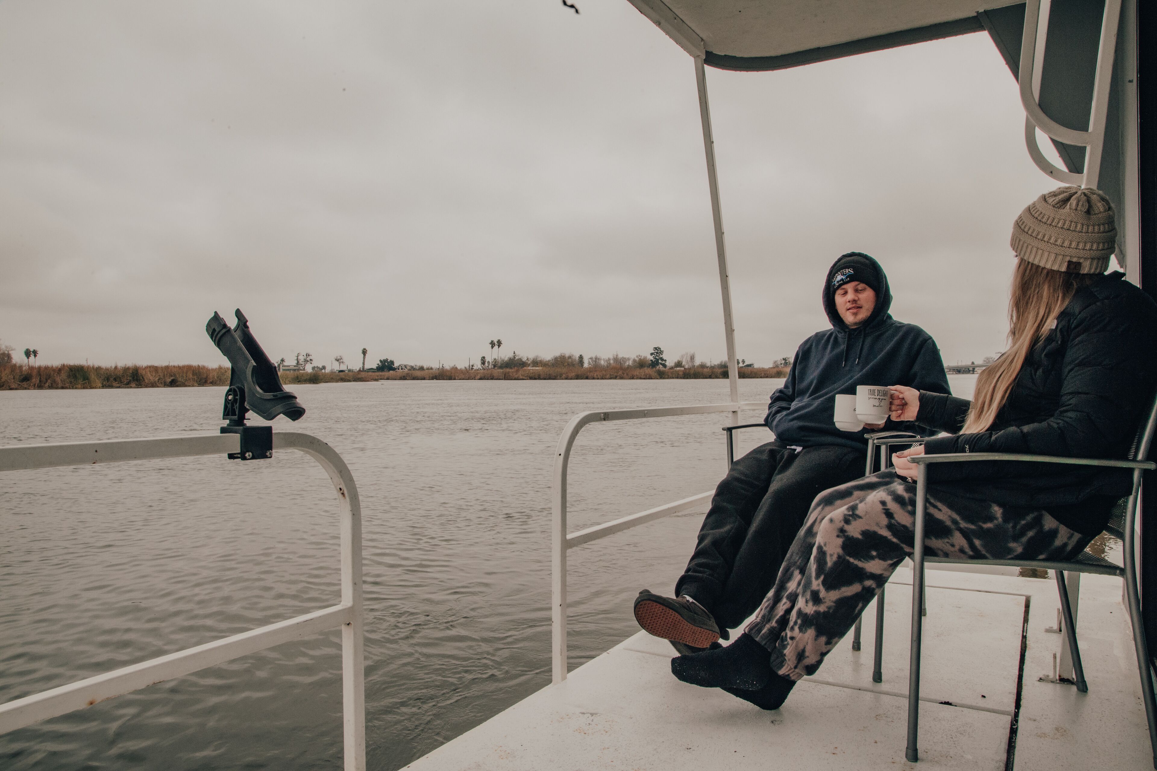 Zwei Personen sitzen auf einem Boot mit Geländer und blicken auf ein Gewässer.