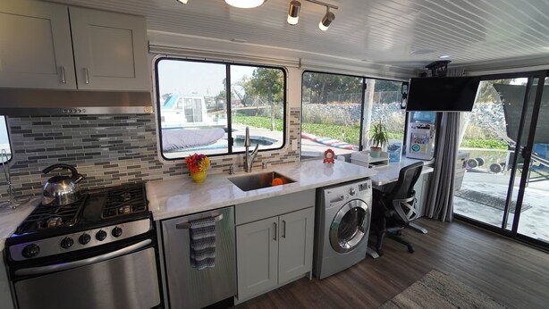 A modern kitchen with a gas stove, a sink, a washing machine, and a large window offering a view of the outdoors. - Romantic Getaway with Sauna, fireplace and great seal watching (Oakley)