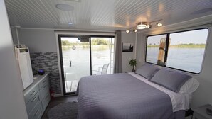 A bedroom with a bed, a desk, a chair, a window with a view of water, and a sliding door to a balcony. - Romantic Getaway with Sauna, fireplace and great seal watching (Oakley)