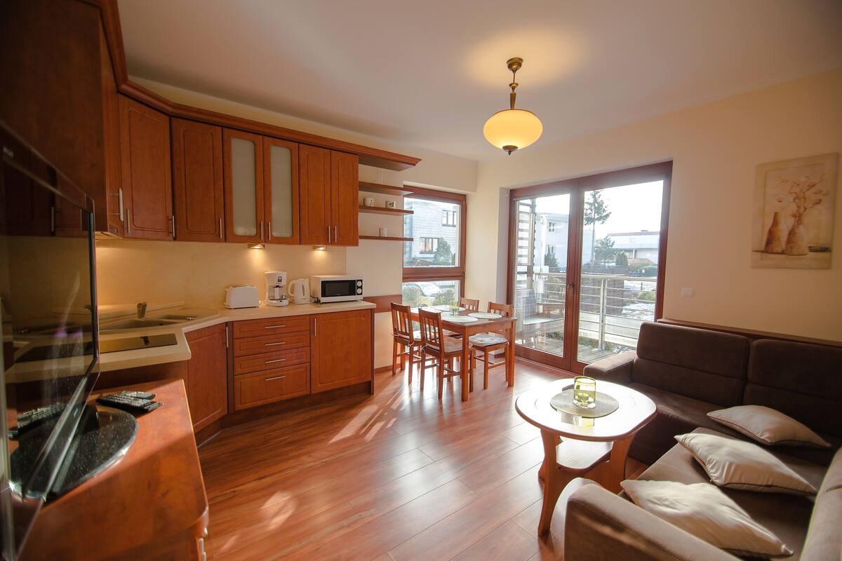 A compact living space with wooden cabinetry, a dining area, a sofa, and a large window providing a view of the outside.