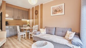 Ein modernes Wohnzimmer mit einer grauen Couch, weißen Stühlen, einem kleinen runden Tisch und einer Küche im Hintergrund.