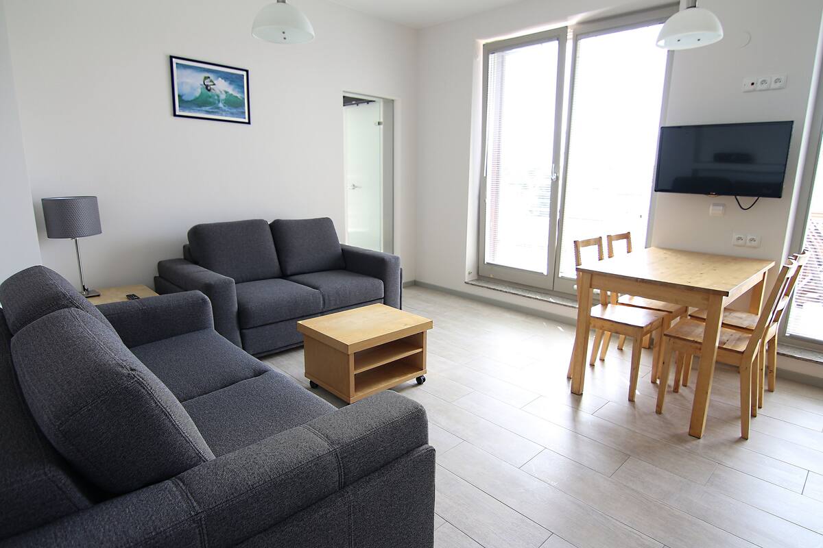 A modern living room with a grey sofa, a wooden coffee table, and a dining area with a table and chairs.