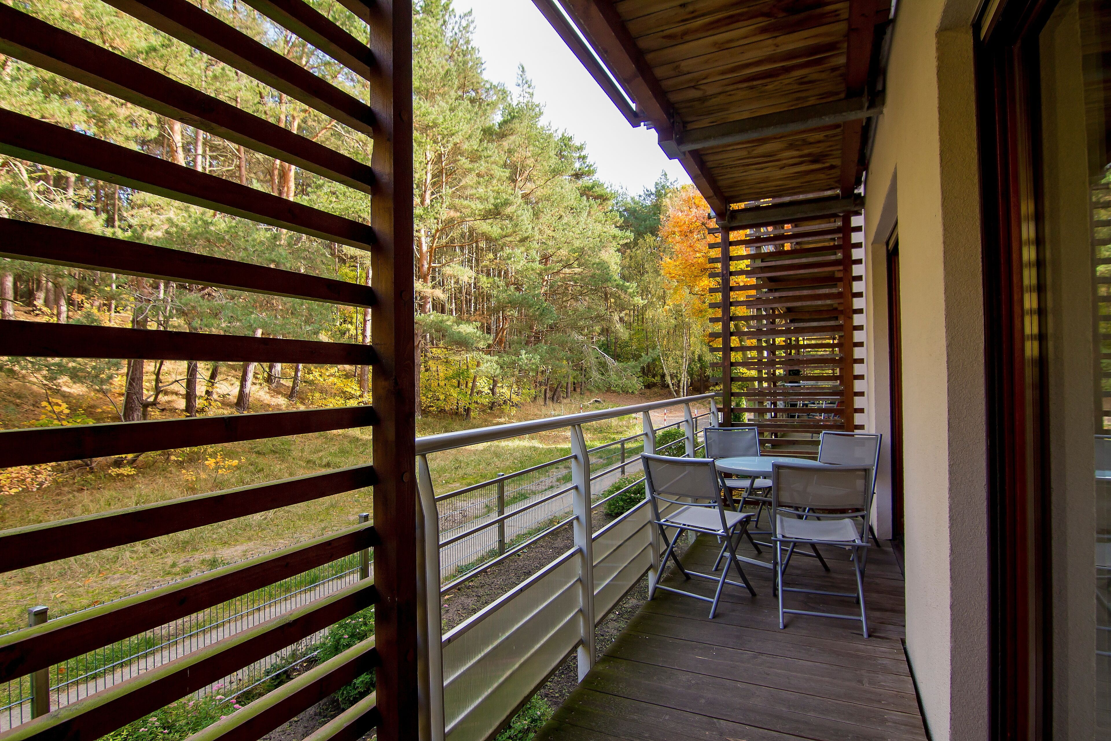 Eine Holzterrasse mit Tisch und Stühlen, mit Blick auf einen bewaldeten Bereich.