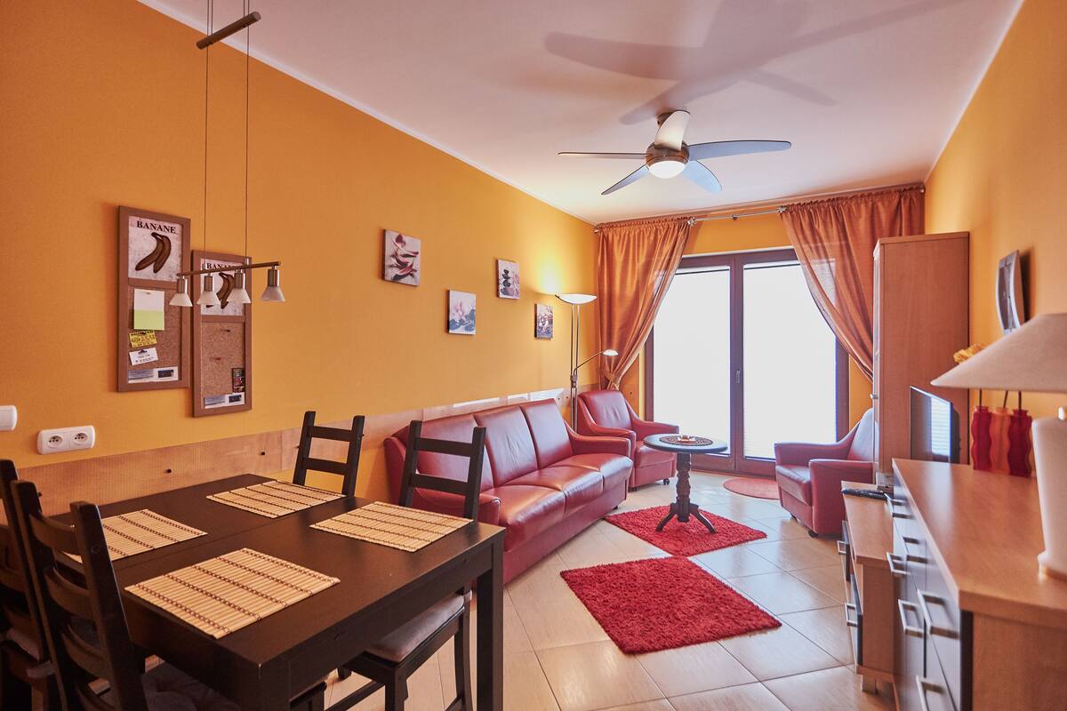 A living room with a dining table, red leather sofa, and a ceiling fan.