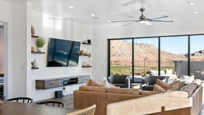A modern living room with a large TV, comfortable seating, and a view of a mountainous landscape. - Ace on the 8th: 2 Private Pools, Sleeps 58! (Washington)