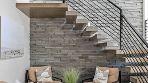 A modern interior with a staircase against a textured wall, a seating area with a coffee table, and a potted plant. - Ace on the 8th: 2 Private Pools, Sleeps 58! (Washington)