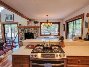 Une cuisine dotée d’une cheminée en pierre, d’une cuisinière à gaz et d’une grande fenêtre donnant sur l’extérieur.