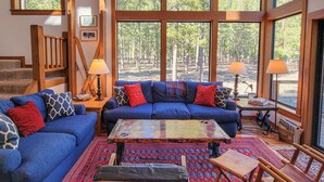 Ein geräumiges Wohnzimmer mit großem Fenster, einem blauen Sofa, einem Couchtisch und einer Treppe.