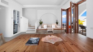 Ein modernes Wohnzimmer mit einem Holzesstisch, einer Couch mit Kissen, einer Treppe und Blick ins Freie.