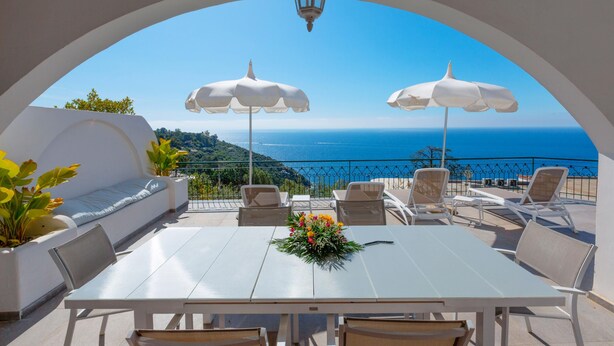 Ein Essbereich im Freien mit Blick auf das Meer, weiße Sonnenschirme und ein Tisch mit floraler Dekoration.