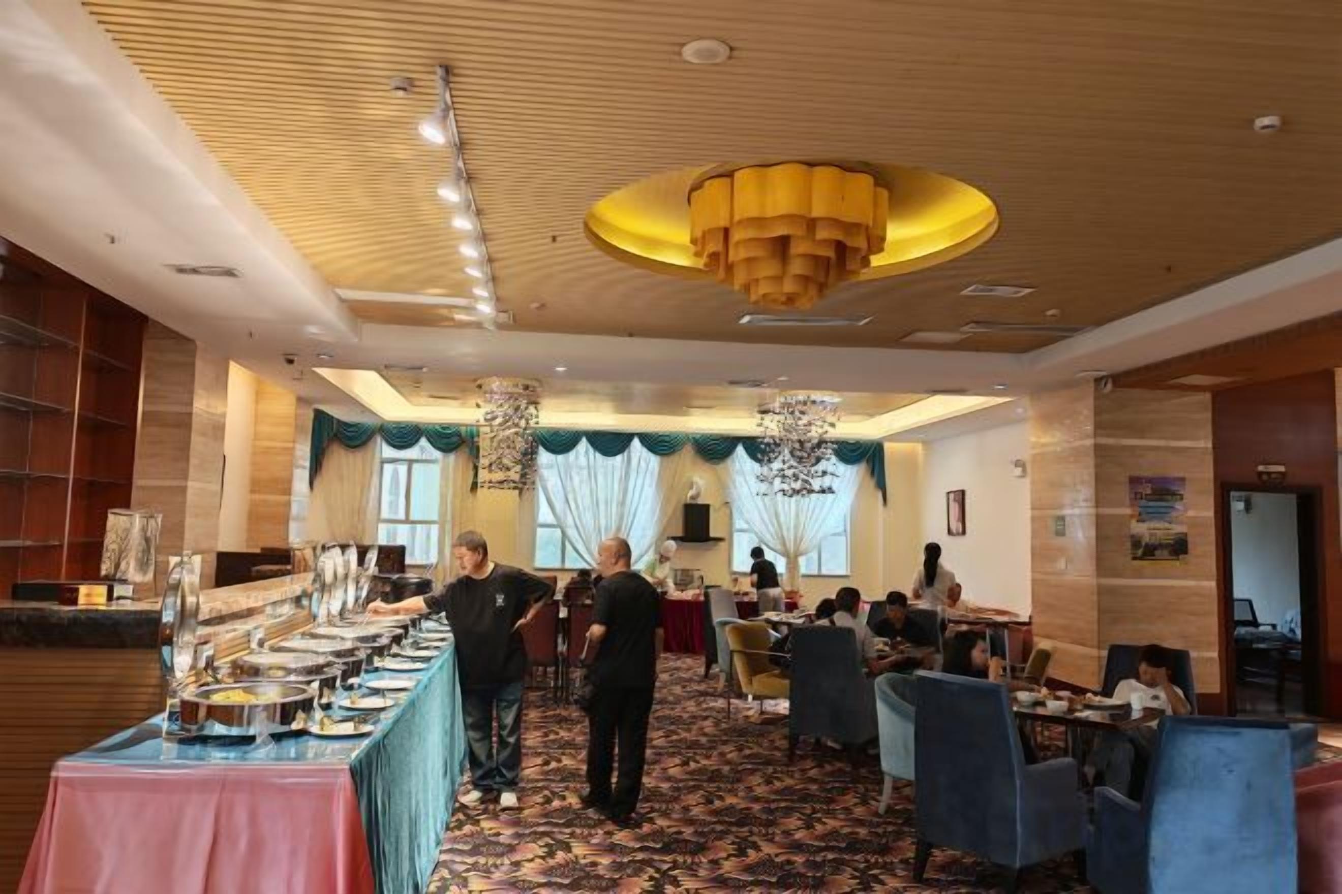 A hotel dining area with a long buffet table, multiple dining tables, and chairs.