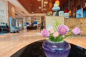 A reception area with a marble counter, a vase with flowers, a reception desk, and a seating area with chairs.