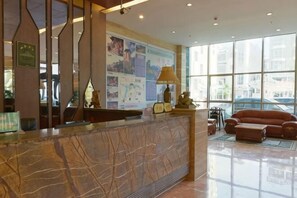 A hotel reception area with a marble counter, a large window, and a red sofa. - Azalea Garden Hotel (Qianxi)
