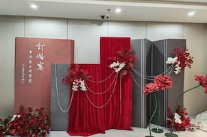 Una habitación con una cortina roja, un panel decorativo con escritura y un arreglo floral.