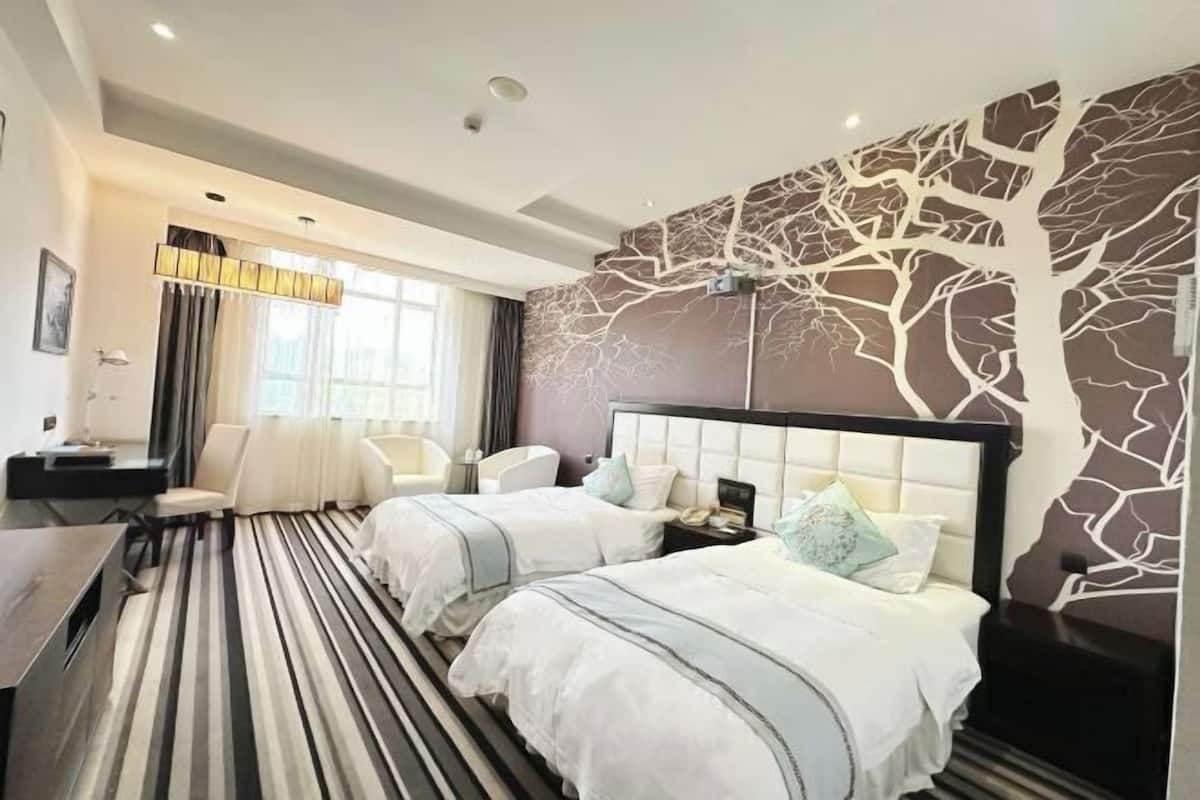 Ett hotellrum med två sängar, ett skrivbord, en stol och ett stort fönster med gardiner.