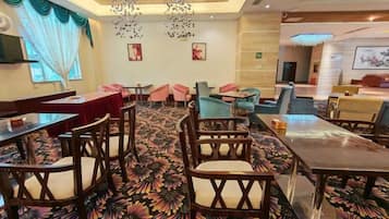 A hotel dining area with tables and chairs, a patterned carpet, and a chandelier.