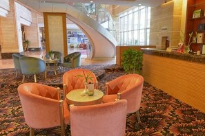 Un vestíbulo con mostrador de recepción curvo, zona de estar con sillones y alfombra estampada.