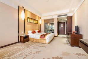 A hotel room with a large bed, a bedside table, a TV, and a view of the hallway. - Azalea Garden Hotel (Qianxi)