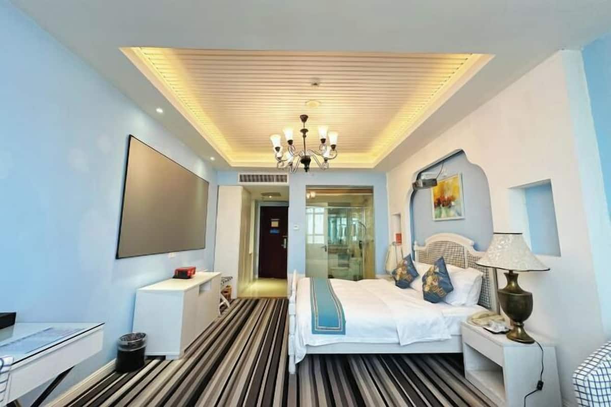 Ett hotellrum med en säng, ett sängbord, en lampa och en stor tv-skärm.