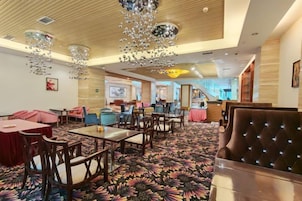 Un hall de hotel con alfombra estampada, techo de madera y diversos arreglos de asientos, incluyendo mesas y sillas.