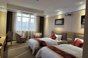 Habitación de hotel con dos camas, un escritorio, una silla y un ventanal amplio.