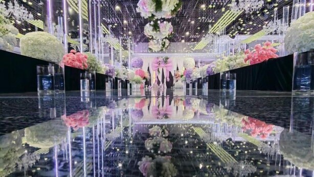 Un salón amplio con piso reflectante, decorado con arreglos florales e iluminación colgante.