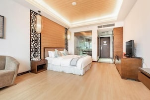 A modern hotel room with a wooden ceiling, a bed with white bedding, a nightstand, a TV on a wooden cabinet, and a glass door leading to a bathroom.