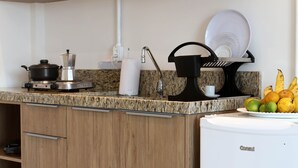 Una cocina con gabinetes de madera, encimera de granito, refrigerador blanco y un escurreplatos con una fuente de fruta.