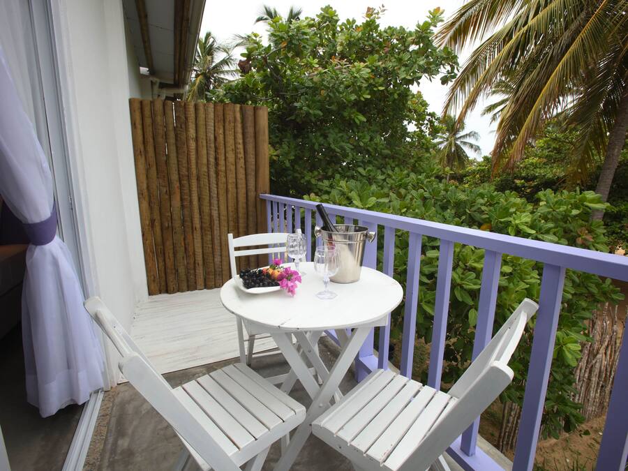 A balcony with a white table, two white chairs, a wooden fence, and lush greenery in the background.
