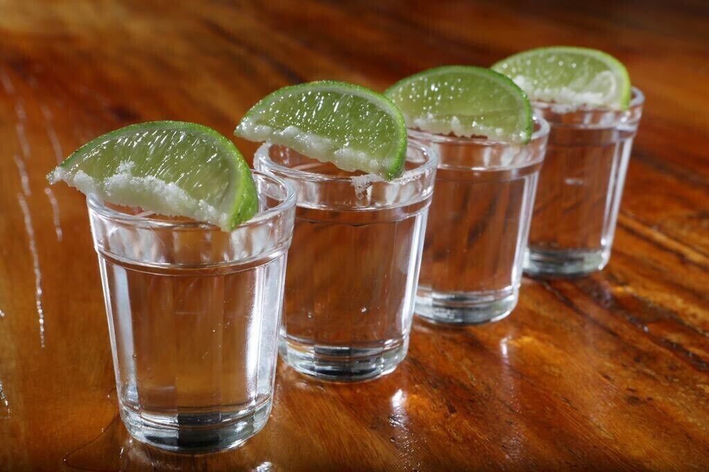 Cuatro vasos de chupito con rodajas de lima sobre una superficie de madera.