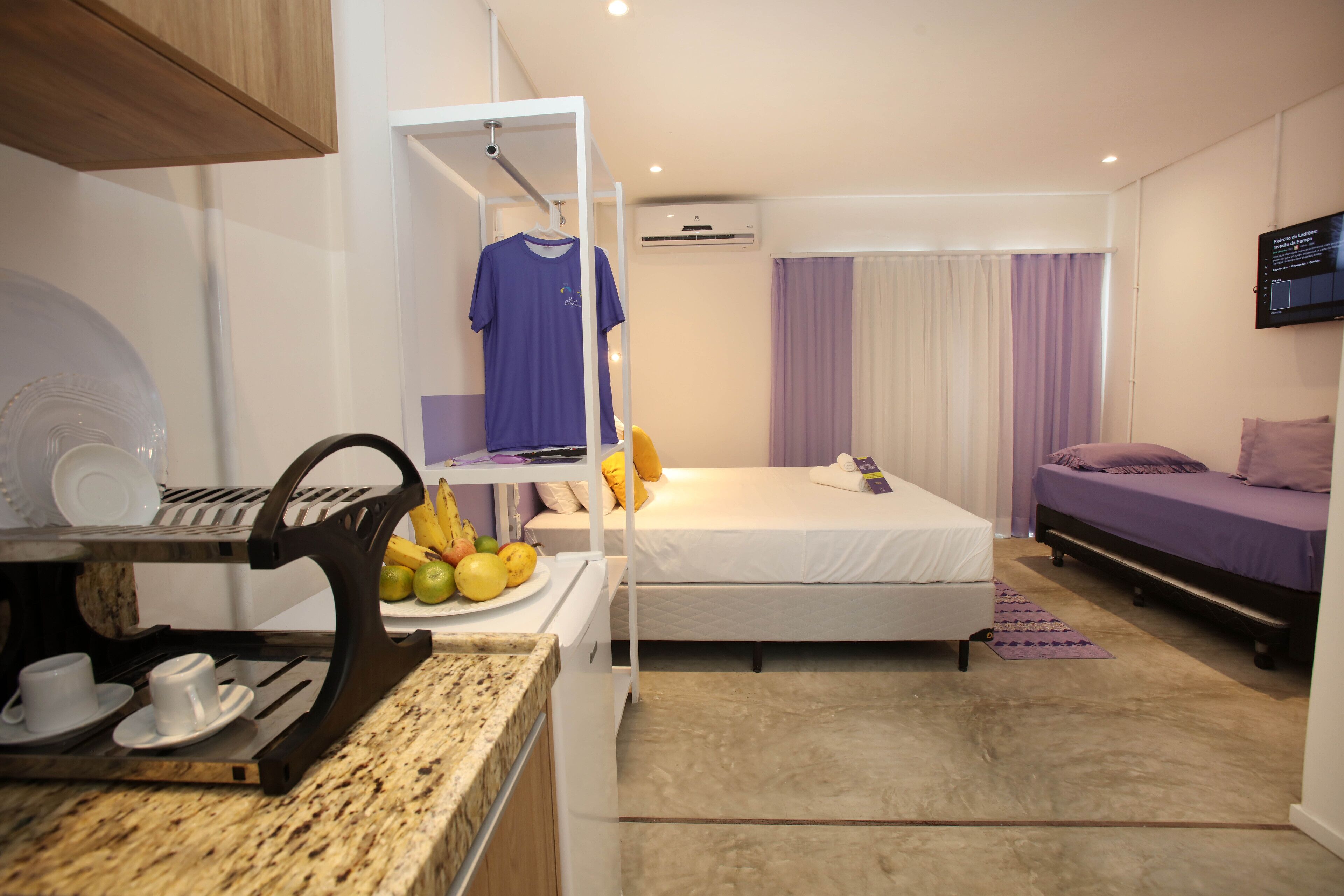 A compact hotel room with a bunk bed, a small kitchenette, and a TV mounted on the wall.