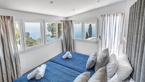 Un dormitorio con cama, dos ventanas y vista al mar.
