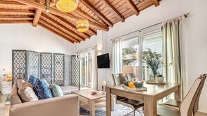 Una sala de estar moderna con techo de madera, un sofá con cojines estampados, una mesa de comedor con sillas y un televisor montado en la pared.
