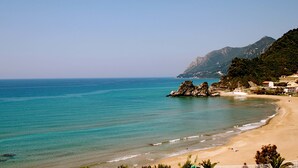 Una playa costera con aguas turquesas cristalinas, afloramientos rocosos y montañas al fondo.