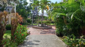 A paved courtyard with a central fountain, surrounded by lush greenery and palm trees. - Large, cosy studio with sea view, pool and beach (Le Gosier)