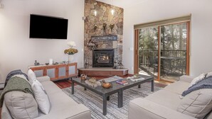 A modern living room with a stone fireplace, a flat-screen TV, and a large sliding glass door to a deck. - Airy Townhome in Vail w/ Beautiful Views, Modern Decor, Free bus shuttle. VP7 (Vail)