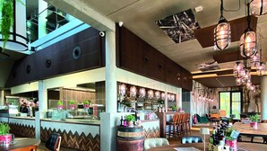 A spacious restaurant with high ceilings, wooden flooring, and a variety of seating arrangements including tables and chairs.