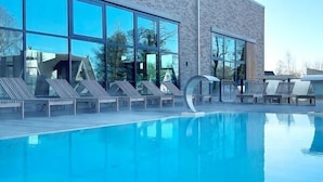 A modern building with a swimming pool, large windows, and lounge chairs.