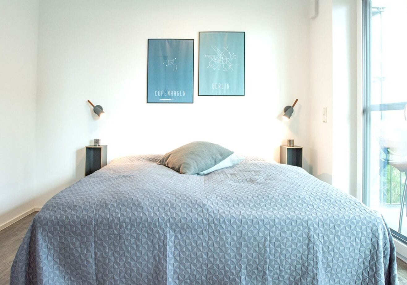 A bedroom with a large bed, two wall-mounted lamps, and two framed city maps.