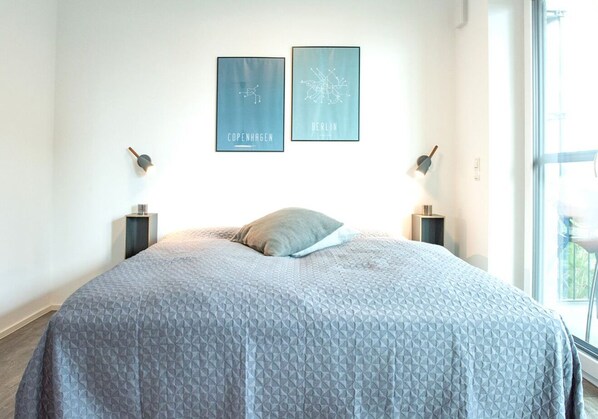 Un dormitorio con una cama grande, dos lámparas fijadas a la pared y dos mapas de la ciudad enmarcados.