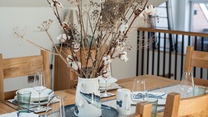 A dining table set with plates, glasses, and a centerpiece of dried branches and cotton. - Church Rooms (Port Isaac)
