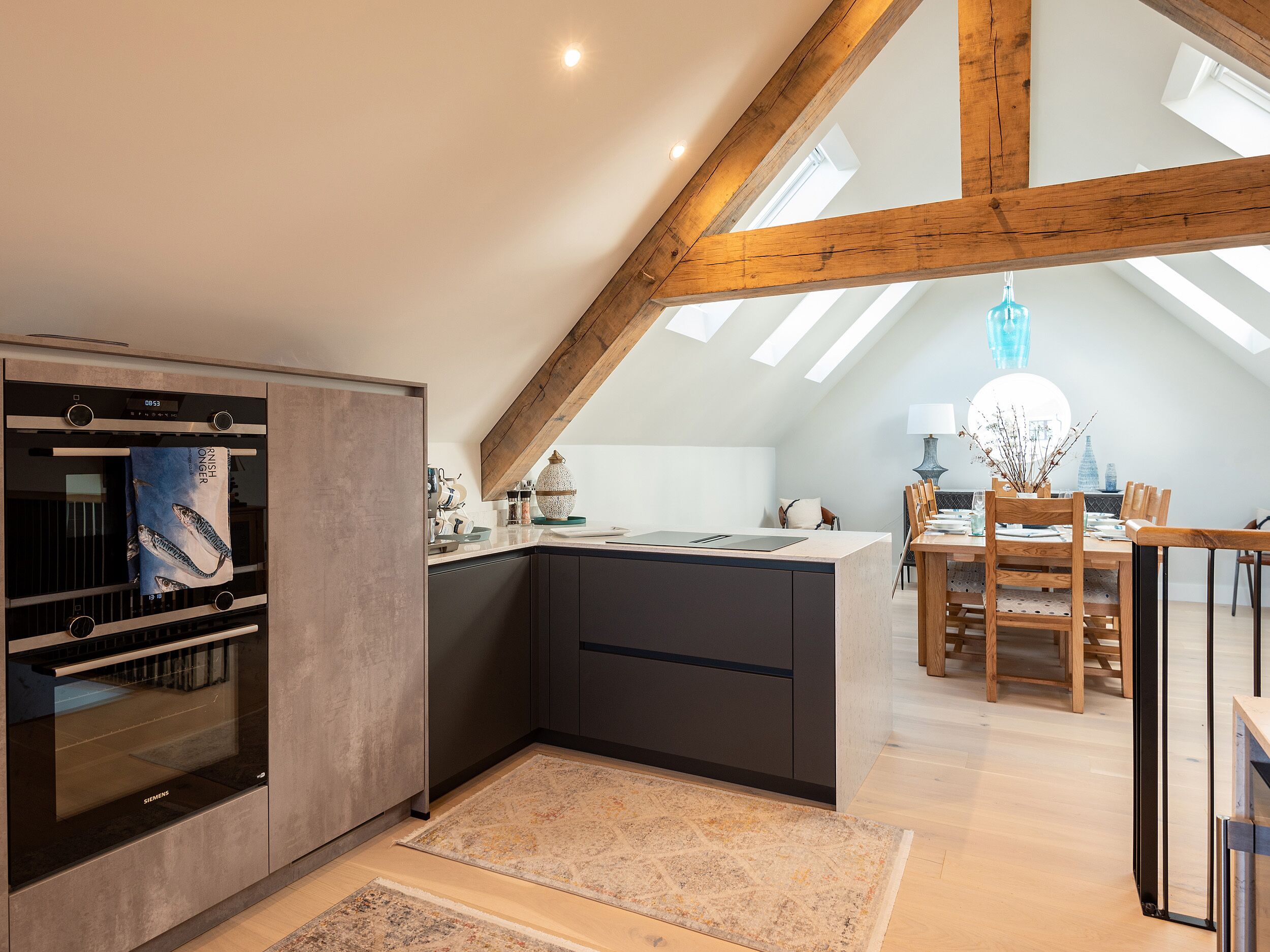 A modern kitchen with a built-in oven, a dining area with a wooden table and chairs, and a skylight.