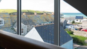 A coastal town view from a window, featuring stone buildings with sloped roofs, a red car, and a solar panel on a roof. - Church Rooms (Port Isaac)