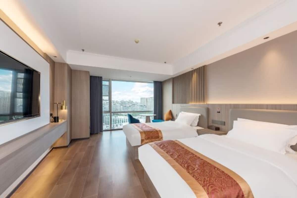 Ein modernes Hotelzimmer mit zwei Betten, einem großen Fenster und Blick auf die Stadt.
