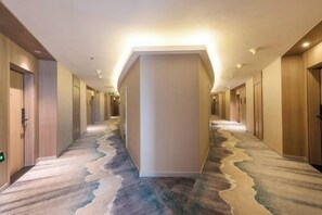 Un pasillo de hotel con piso alfombrado, puertas a ambos lados y un pilar central.