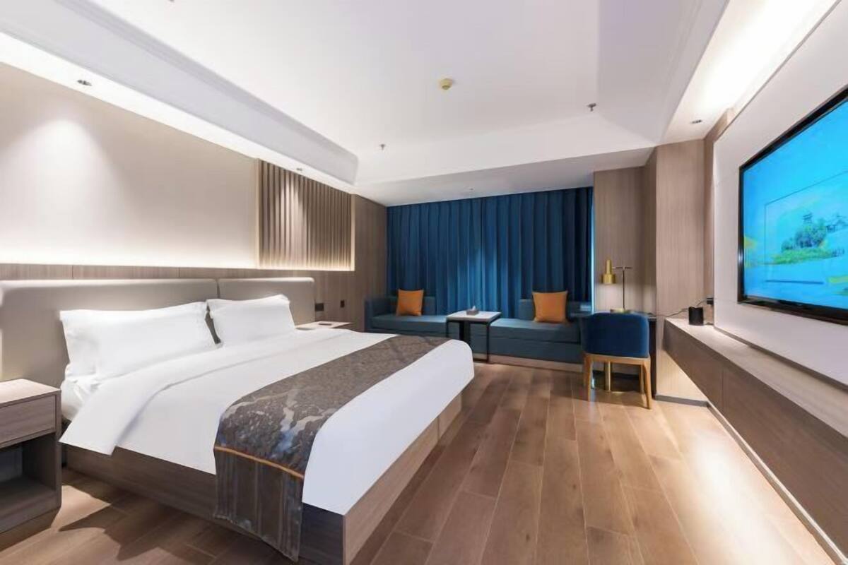 Ein modernes Hotelzimmer mit einem großen Bett, einer Sitzecke mit Sofa und Sesseln, einem kleinen Tisch und einem an der Wand befestigten Fernseher.